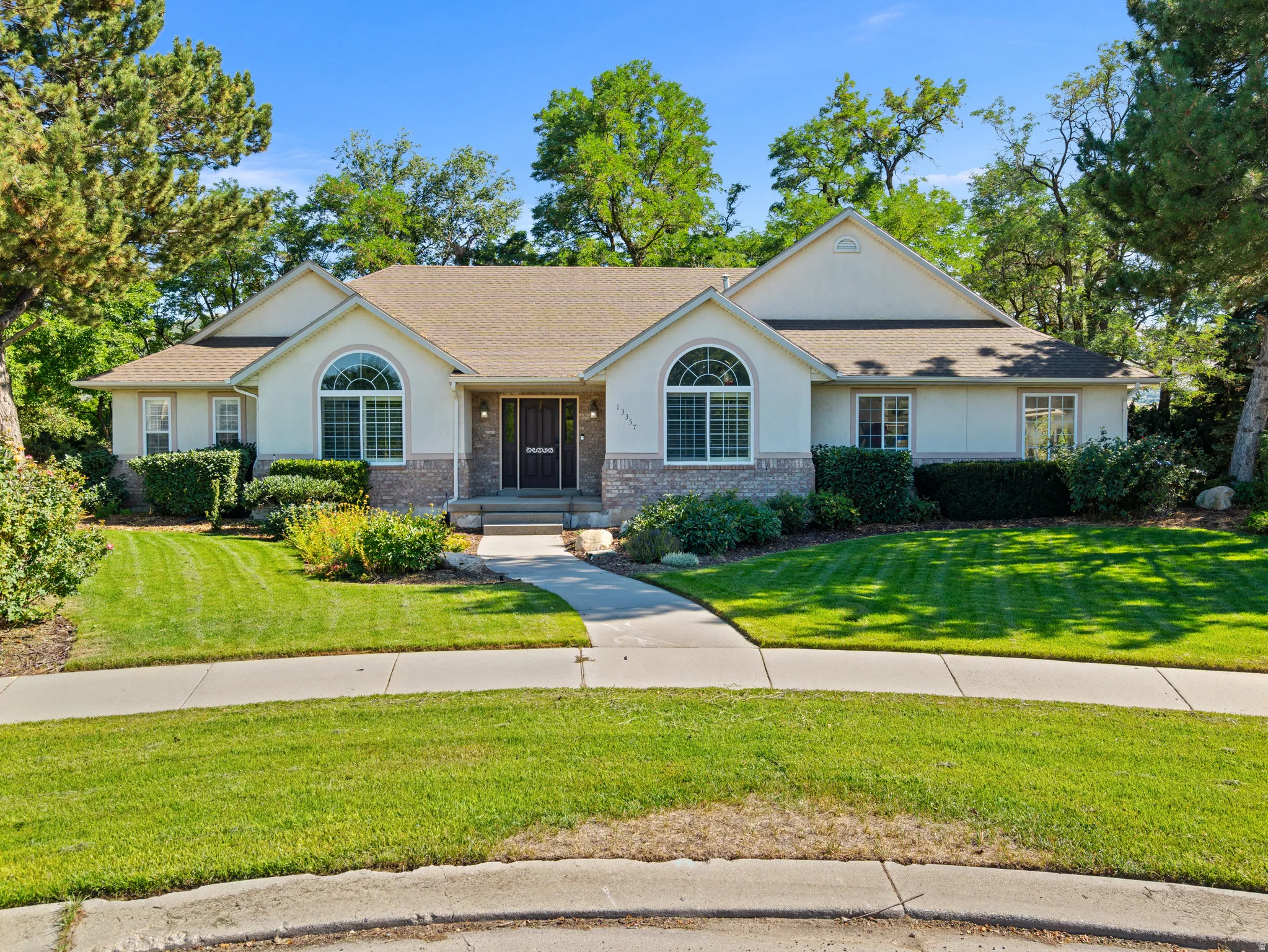 Ranch-style residence featuring a stucco and stone facade, arched window details, a prominent entry, concrete walkway, and a manicured lawn