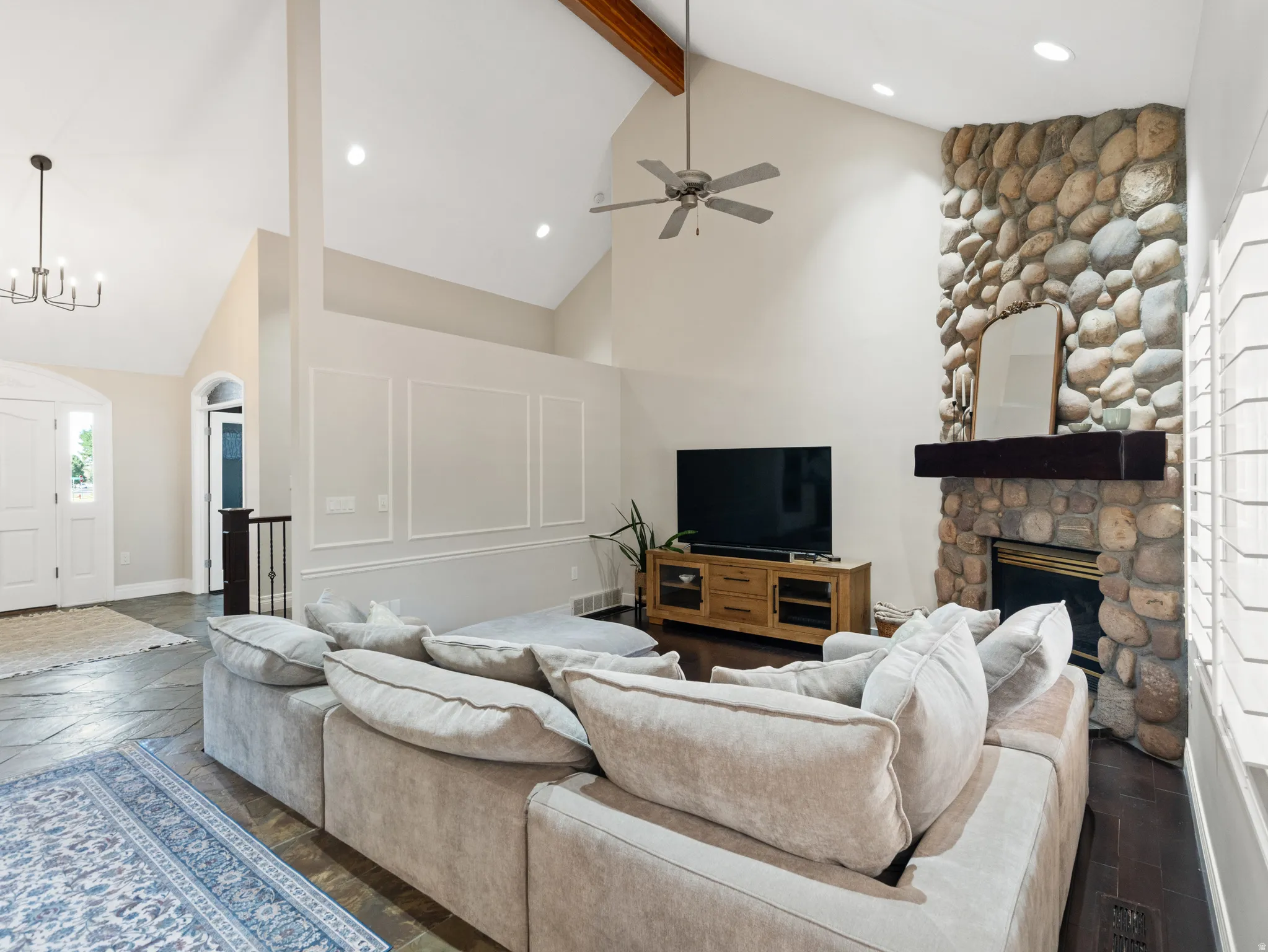 Vaulted ceiling living area featuring a stone-clad fireplace with a wood mantel, exposed wood beam, recessed lighting, and wall panel molding