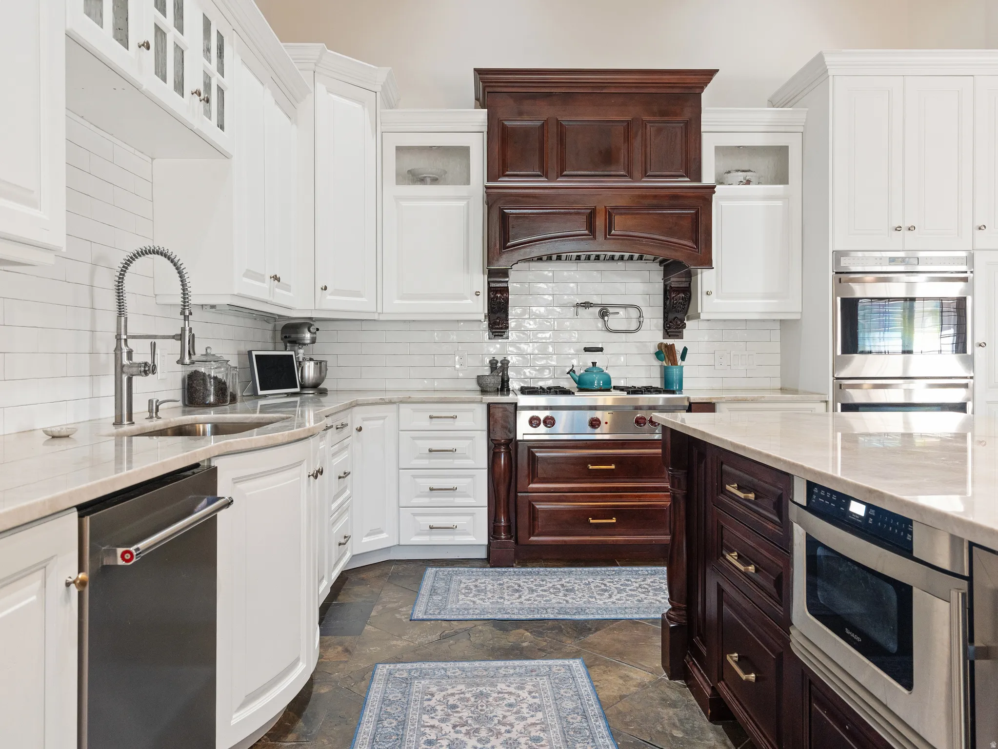 Gourmet kitchen featuring a wood range hood, stainless steel appliances, white cabinetry, a large center island, and stone flooring