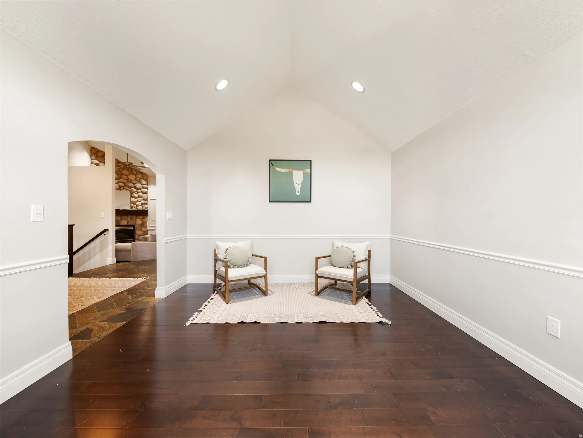 Vaulted ceiling with recessed lighting, dark wood-finish flooring, white walls with chair rail and baseboard molding, and an arched entryway