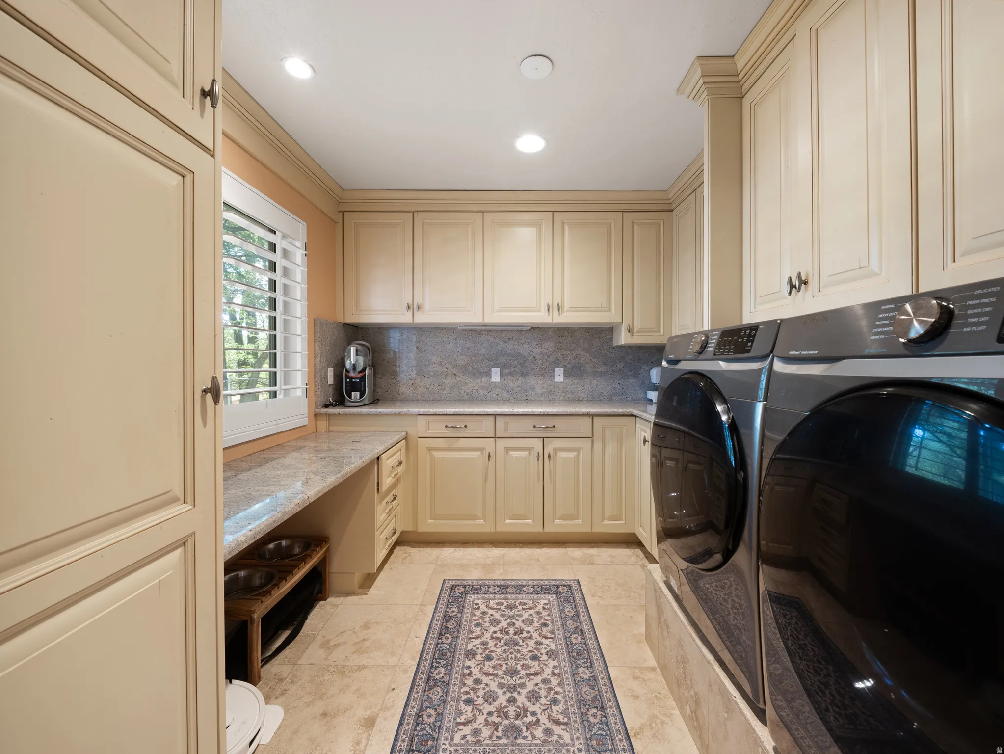 Laundry area featuring extensive cream-colored cabinetry, stone countertops, and a full-height tile backsplash