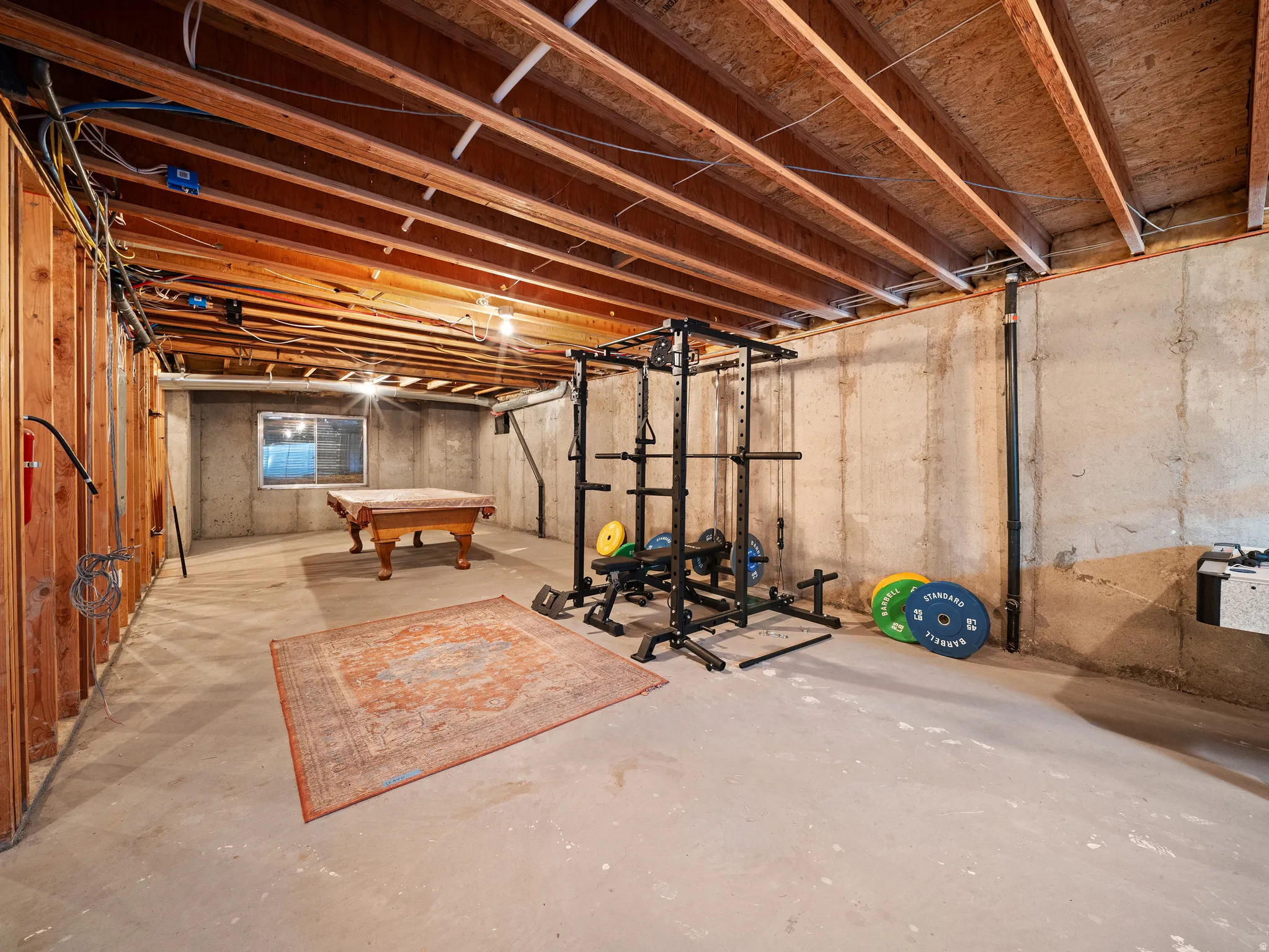 Unfinished basement featuring exposed wood joists, concrete foundation walls, and a visible window