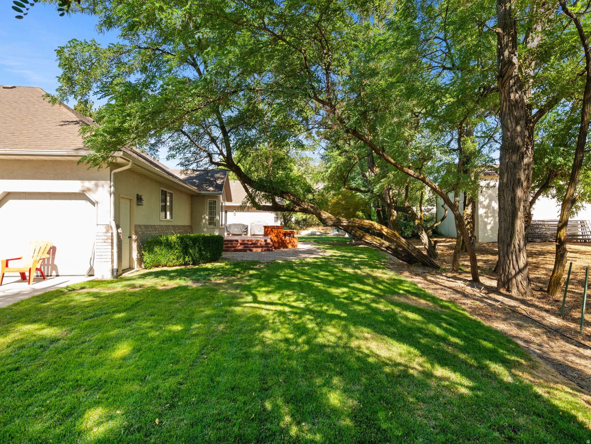 Expansive rear yard featuring mature trees, a manicured lawn, and a brick patio with a built-in fire pit