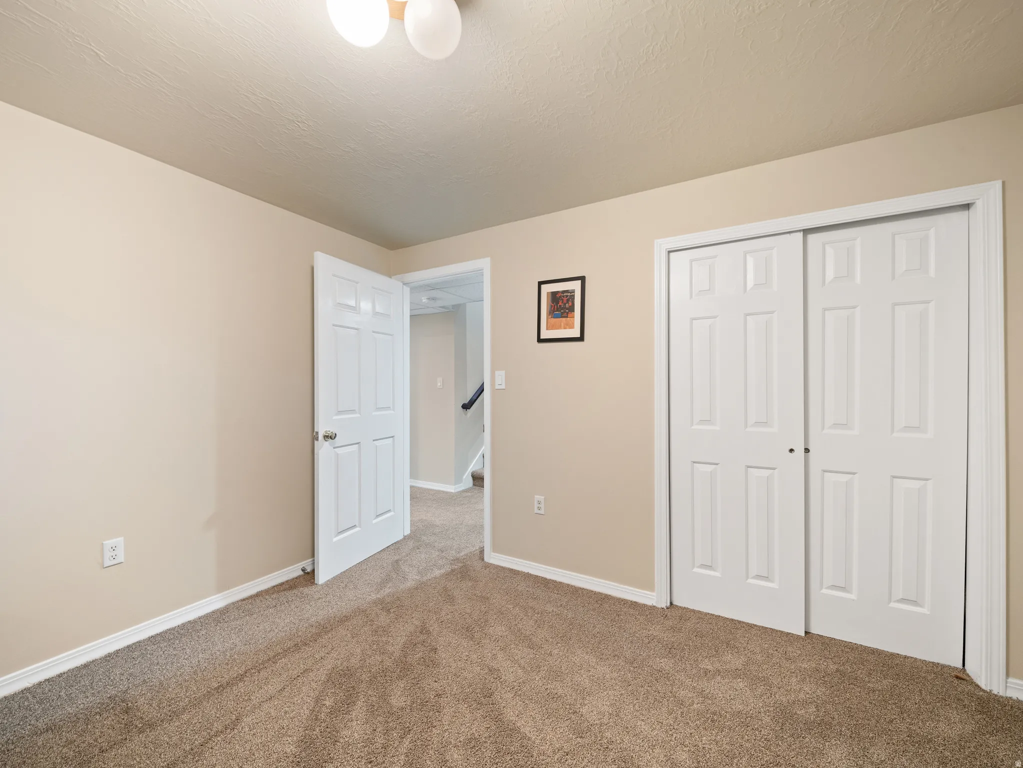 Carpeted room featuring beige walls, white baseboards, a six-panel door, and a two-door bypass closet