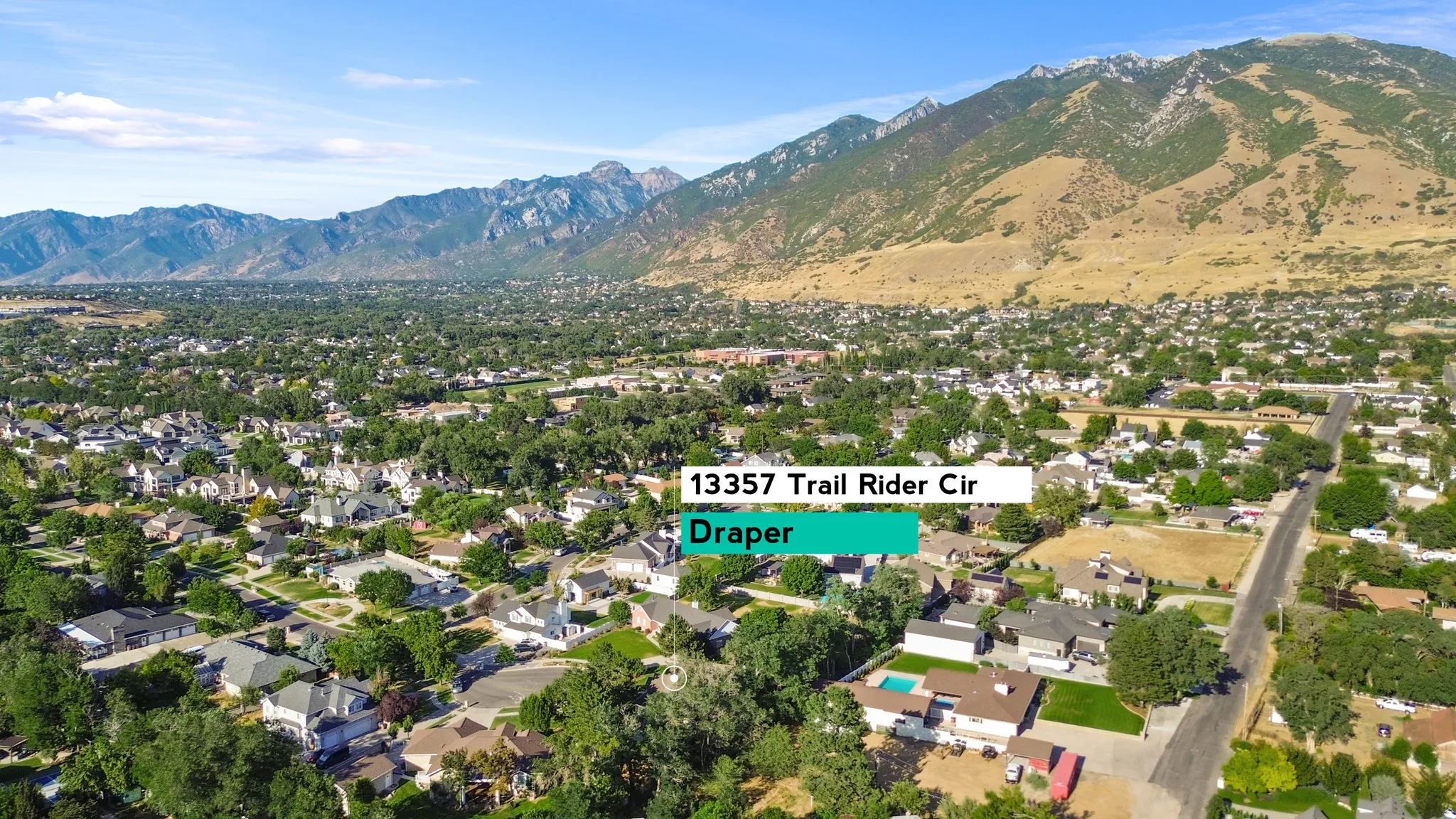 Suburban neighborhood featuring varied residential architecture, mature trees, and mountainous backdrops