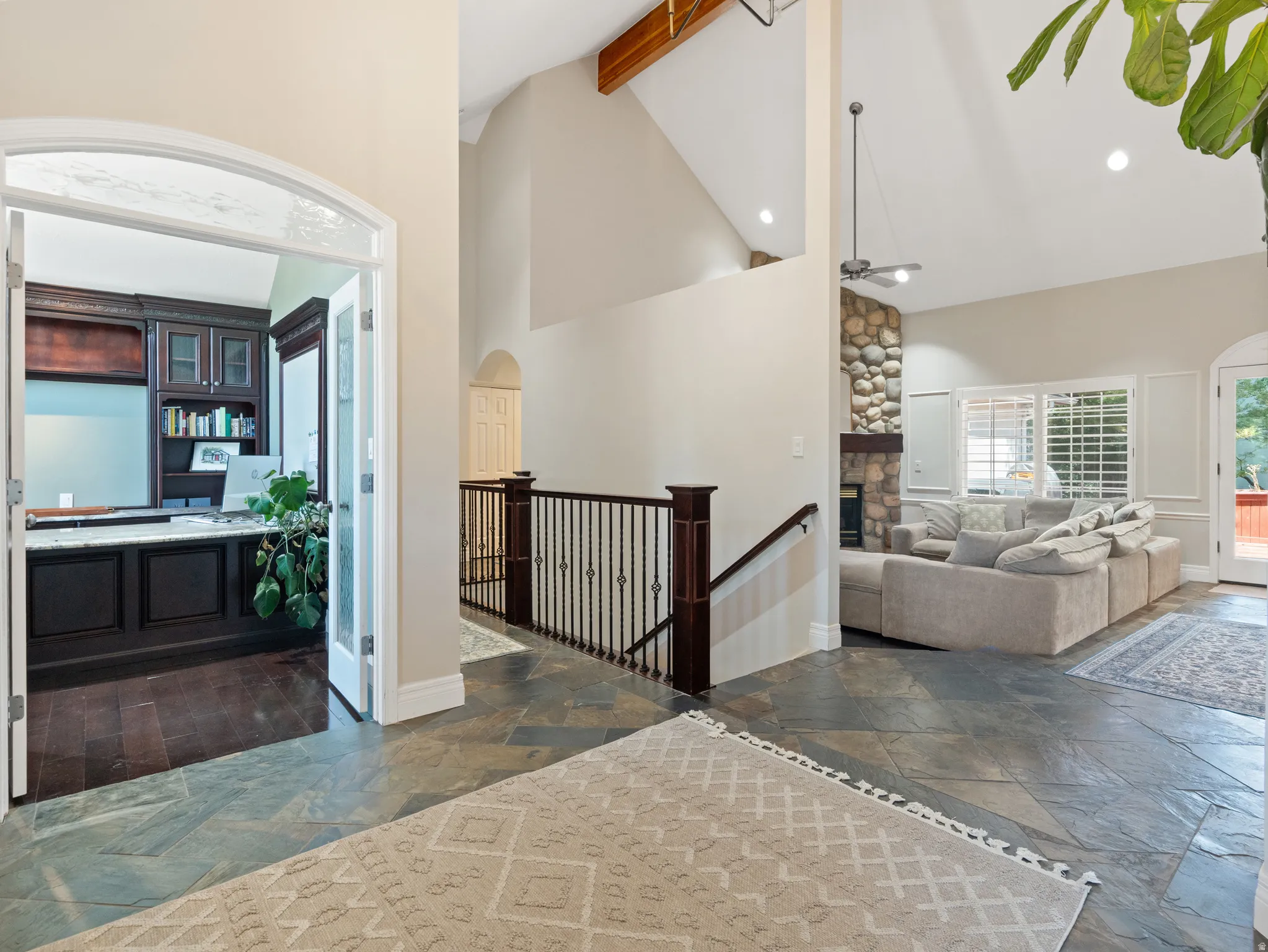 Spacious entry featuring natural stone flooring, an arched doorway, and a wrought iron railing leading to an open living area