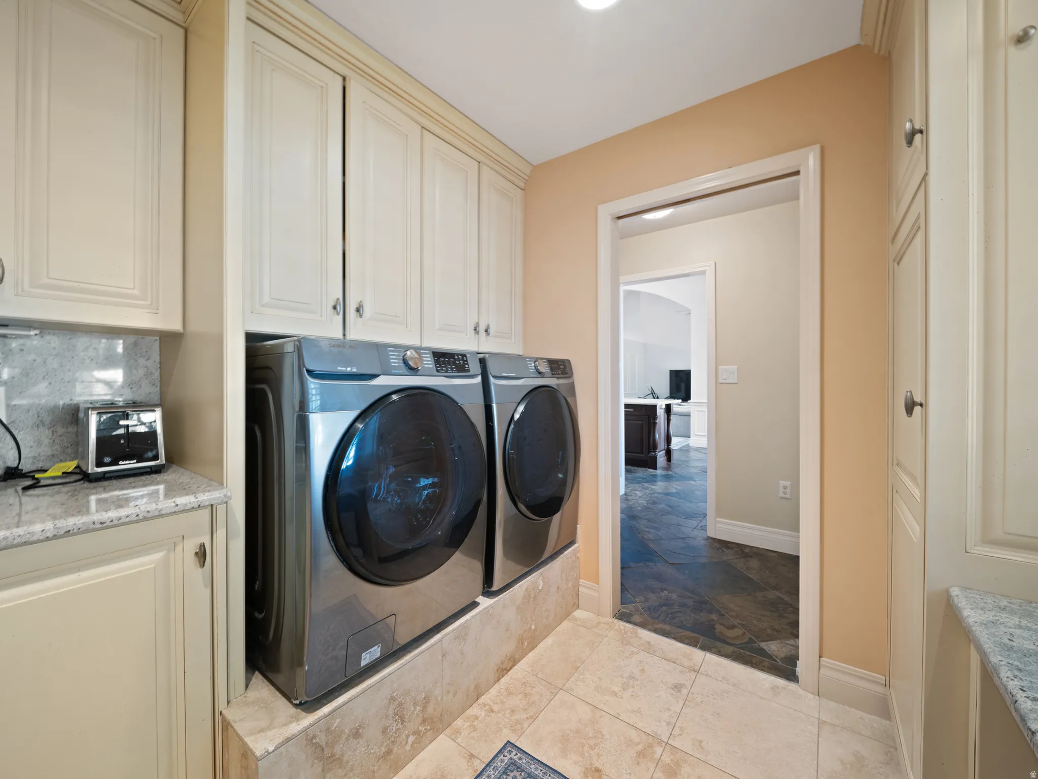 Laundry area featuring extensive built-in cabinetry, tiled flooring, countertop space, and a stone backsplash