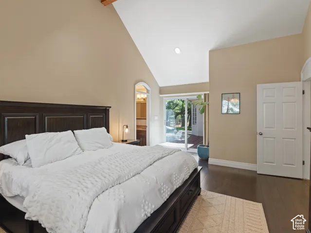 Vaulted ceiling with exposed wood beam, dark wood-finish flooring, sliding glass door access to a patio, and an arched entry