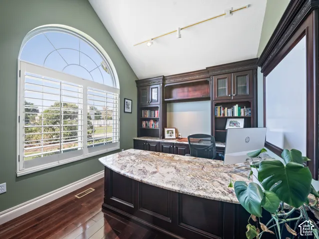 Arched window with plantation shutters, featuring a built-in desk with a stone countertop, custom cabinetry, and hardwood flooring