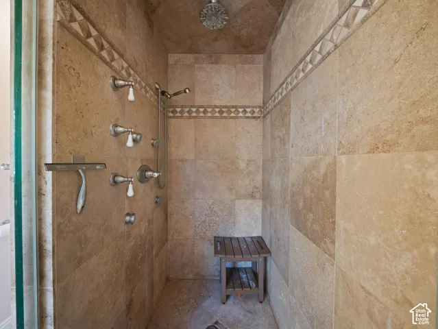 Tiled shower stall featuring multiple shower heads, a handheld shower fixture, and decorative accent tiling