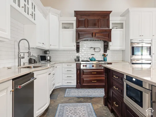 Gourmet kitchen featuring a wood range hood, stainless steel appliances, white cabinetry, a large center island, and stone flooring