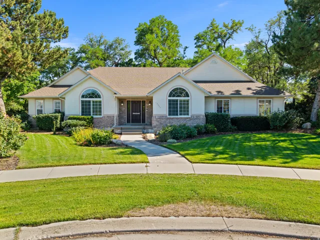 Ranch-style residence featuring a stucco and stone facade, arched window details, a prominent entry, concrete walkway, and a manicured lawn