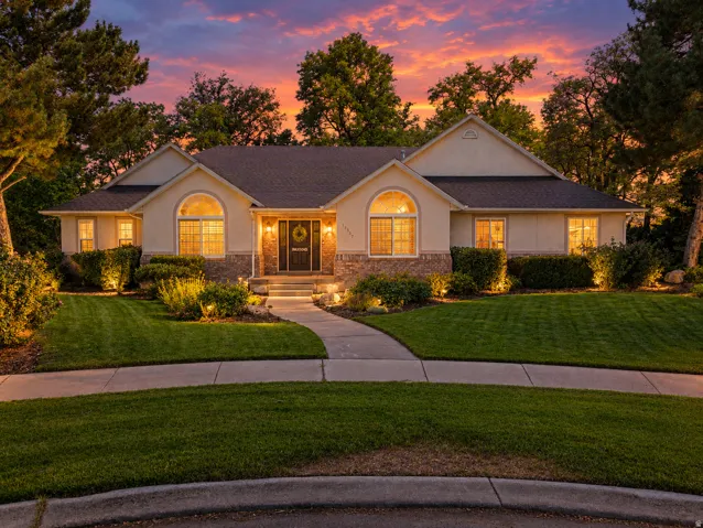 Stucco and stone exterior with arched window accents, established landscaping, and a concrete pathway
