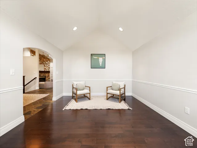 Vaulted ceiling with recessed lighting, dark wood-finish flooring, white walls with chair rail and baseboard molding, and an arched entryway