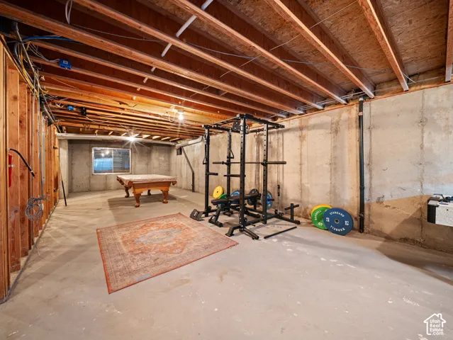 Unfinished basement featuring exposed wood joists, concrete foundation walls, and a visible window