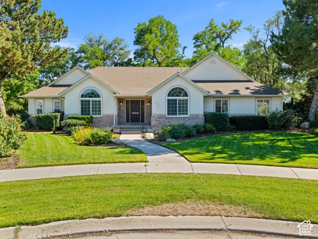 Ranch-style residence featuring a stucco and stone facade, arched window details, a prominent entry, concrete walkway, and a manicured lawn