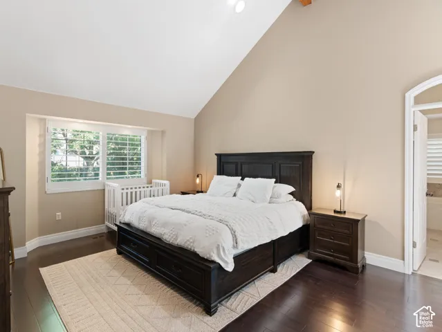 Spacious room featuring vaulted ceilings, dark wood-finish flooring, and a large window with white plantation shutters