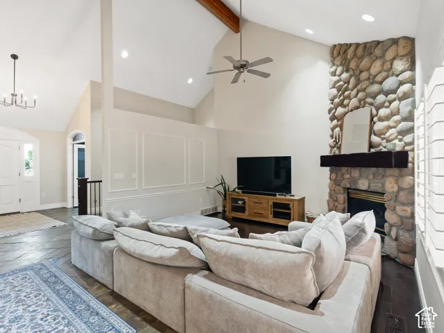Vaulted ceiling living area featuring a stone-clad fireplace with a wood mantel, exposed wood beam, recessed lighting, and wall panel molding