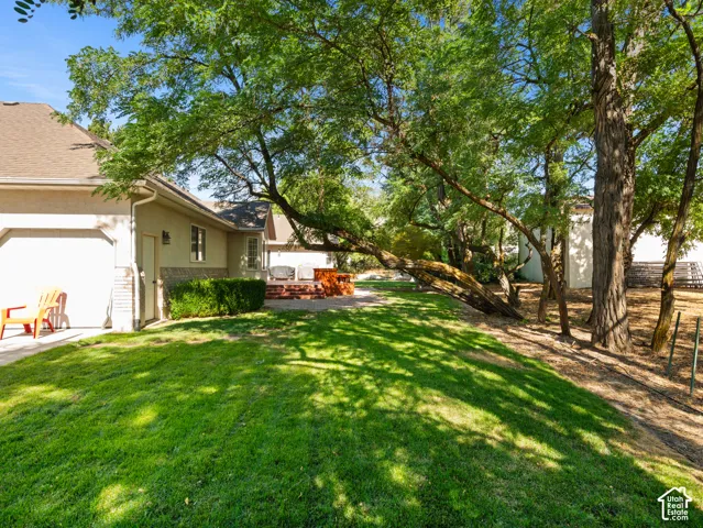 Expansive rear yard featuring mature trees, a manicured lawn, and a brick patio with a built-in fire pit