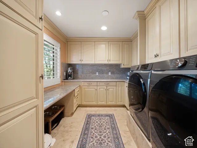 Laundry area featuring extensive cream-colored cabinetry, stone countertops, and a full-height tile backsplash