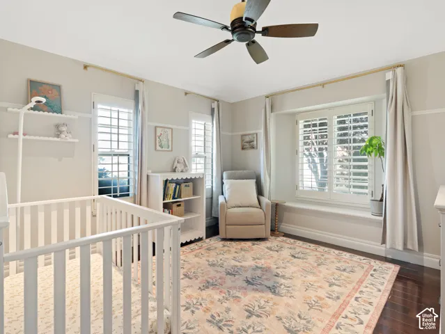 Well-appointed room featuring dark wood-finish flooring, a ceiling fan, and multiple windows with plantation shutters