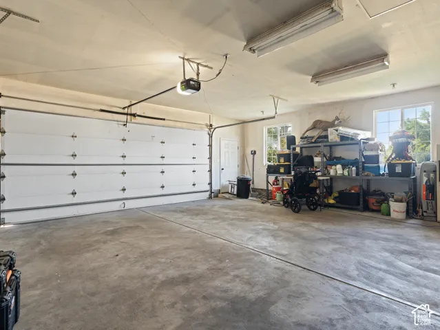 Spacious garage featuring a concrete floor, overhead fluorescent lighting, two windows, and a side entry door