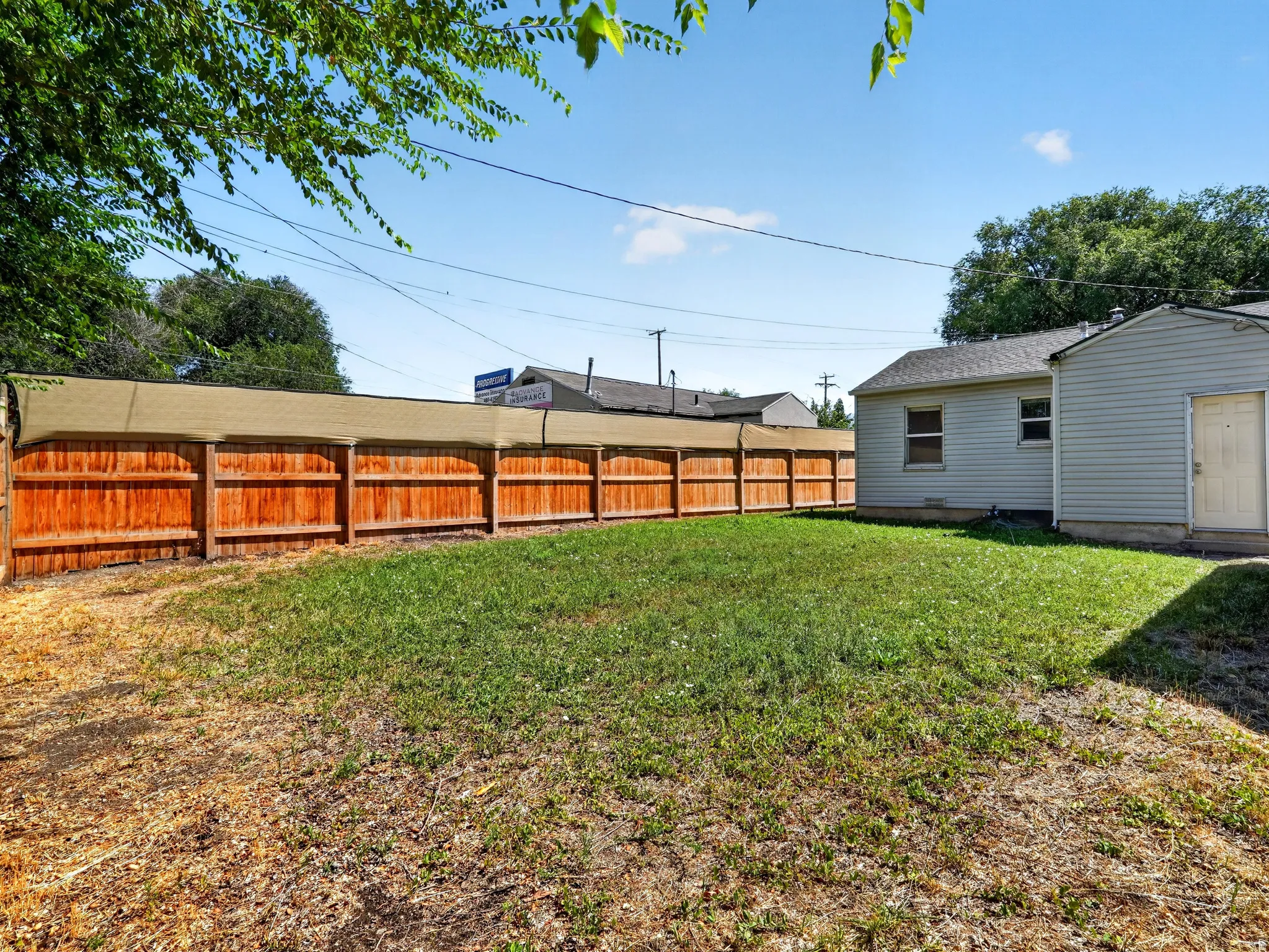 Expansive backyard featuring a wood privacy fence topped with a shade screen, a partial view of the property's exterior siding, and a grass lawn