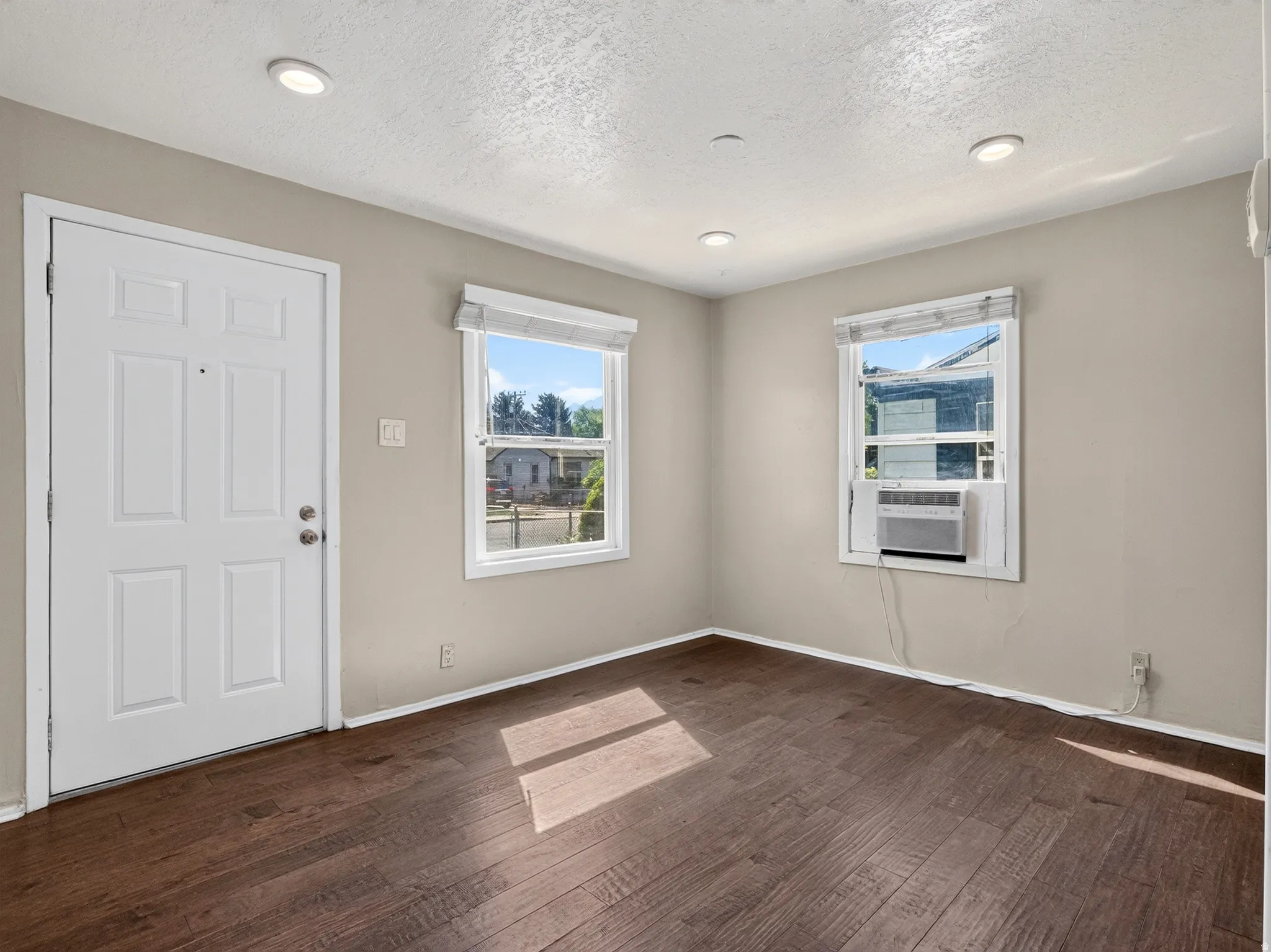 Living space featuring wood-finish flooring, two windows, recessed lighting, and a paneled entry door