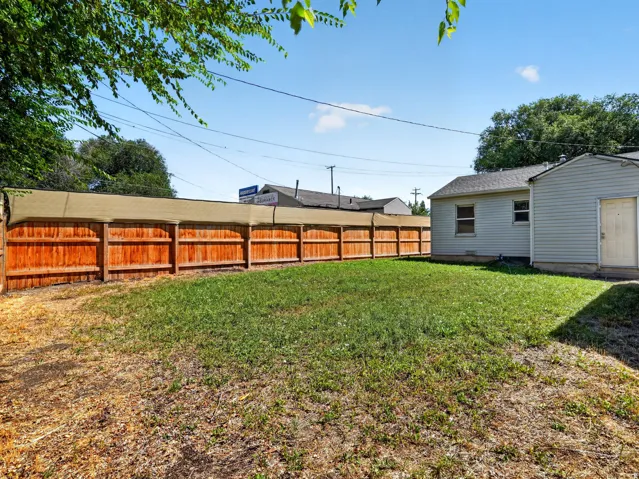 Expansive backyard featuring a wood privacy fence topped with a shade screen, a partial view of the property's exterior siding, and a grass lawn