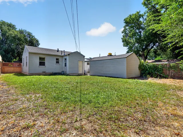 Expansive backyard featuring a detached storage shed, privacy fencing, mature trees, and a rear exterior with horizontal siding and a gabled roof