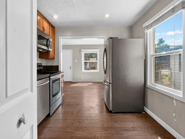 Kitchen featuring wood-finish flooring, stainless steel appliances, wood cabinetry, dark countertops, and a window with blinds