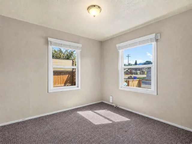 Room featuring two windows, neutral painted walls, and textured carpet flooring