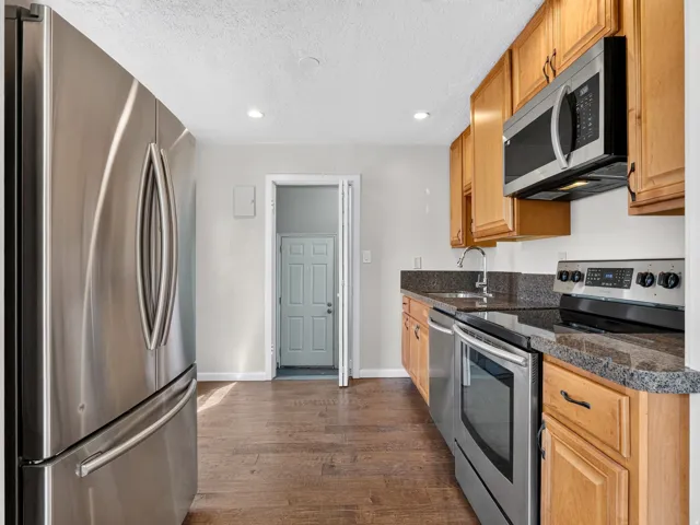 Kitchen featuring wood-finish flooring, stainless steel appliances, wood cabinetry, stone countertops, and recessed lighting
