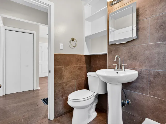 Bathroom featuring a pedestal sink, a toilet, a wall-mounted medicine cabinet, built-in shelving, and floor-to-ceiling tile