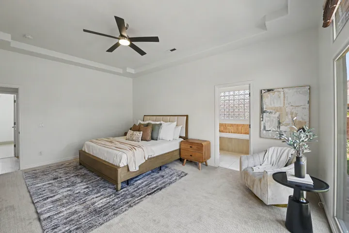 Spacious room featuring tray ceilings with a ceiling fan, light-toned carpeting, and a large window offering natural light