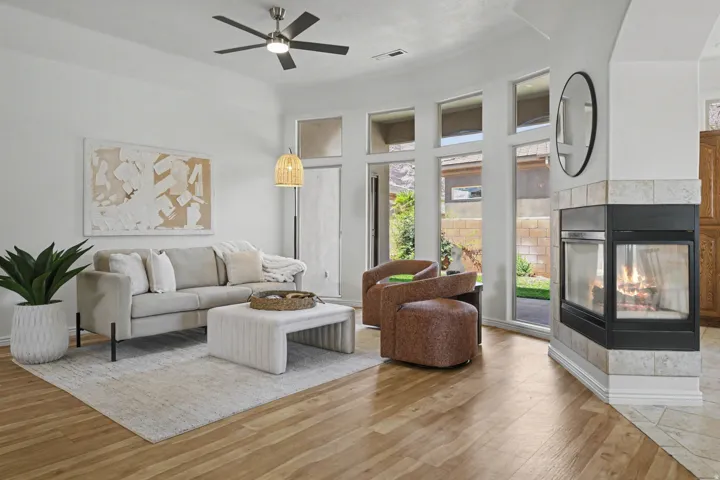 Living area featuring wood-finish flooring, a corner fireplace with light-toned tile surround, and multiple tall windows providing ample natural light