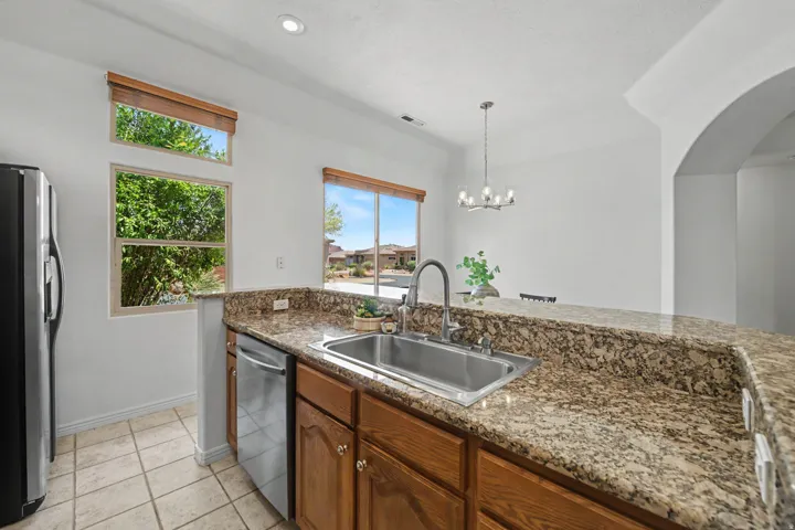 Kitchen featuring granite-style countertops, an undermount stainless steel sink with a high-arc faucet, wood-finish cabinetry, and stainless steel appliances including a refrigerator and dishwasher