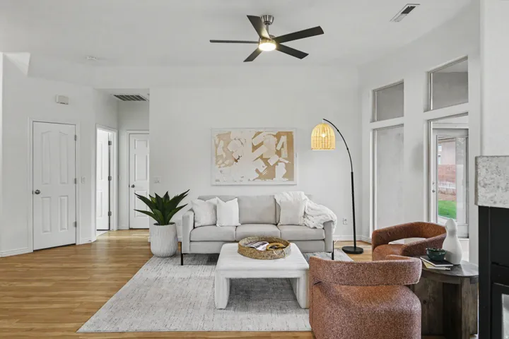 Bright living area with wood-finish flooring, a contemporary ceiling fan, and white walls