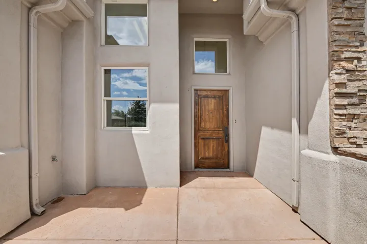 Entryway featuring a solid wood door with dark hardware, stucco exterior, stacked stone accent, and multiple windows