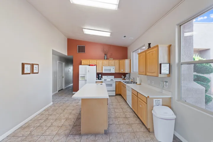 Spacious kitchen featuring wood-finish cabinetry, a large center island with prep space, stainless steel appliances including refrigerator and range, tile flooring, and abundant natural light from multiple windows