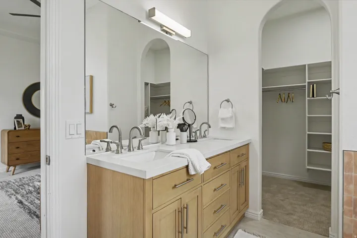 Primary Bathroom Vanity featuring a dual-sink white quartz countertop, wood-finish cabinetry with multiple drawers and storage, chrome widespread faucets, and a large frameless mirror with integrated lighting