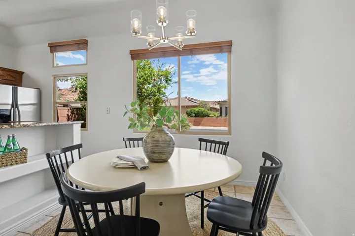 Dining area featuring a modern chandelier, multiple windows with wood-tone trim, a built-in breakfast bar with a granite-style countertop, stainless steel appliances, and tile flooring