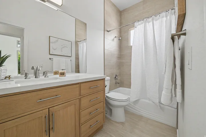 Spa-inspired primary bathroom featuring a wood-finish vanity with dual sinks, white quartz countertop, and polished chrome fixtures