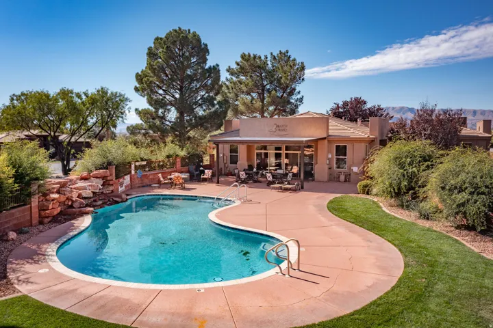 Curved swimming pool with a rock waterfall feature, extensive pool decking, and surrounding green lawn