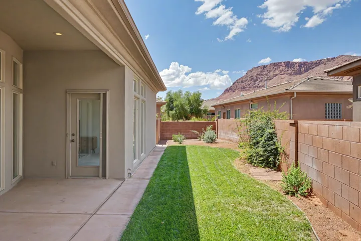 Covered concrete patio with recessed lighting, offering direct access to a private backyard with a manicured lawn and red rock mountain backdrop