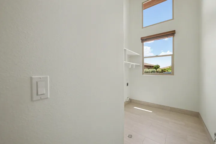 Utility area featuring high ceilings, a large window with a wood-finish blind, and an upper transom window