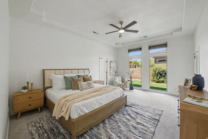 Spacious room featuring a tray ceiling, ceiling fan, and large windows with integrated blinds
