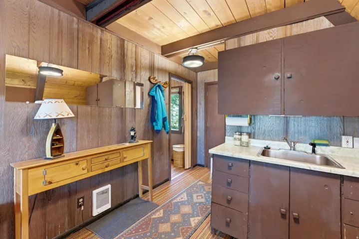 Wood-paneled interior featuring a compact utility sink area with brown cabinetry, a rectangular stainless steel sink, and a light-colored countertop