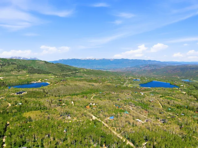 Expansive aerial showcasing a mountainous landscape with multiple lakes, dense tree coverage, and scattered residential properties