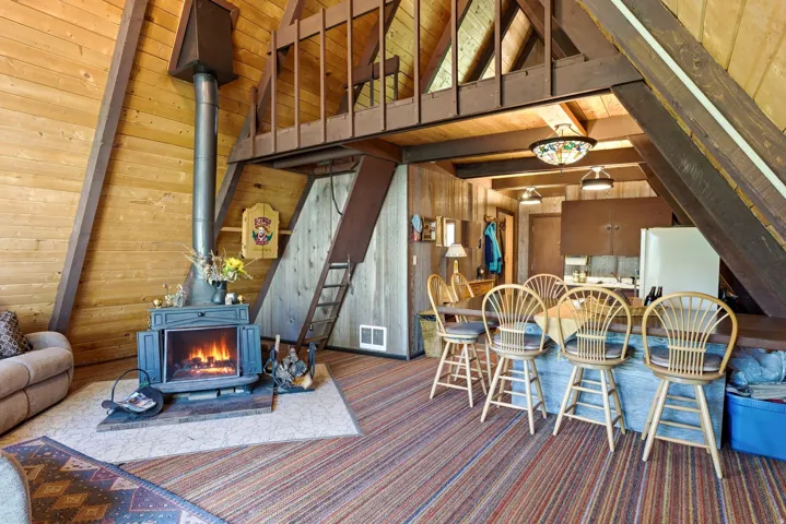 A-frame interior with wood-finish walls and ceilings, featuring a central wood-burning stove with a metal chimney